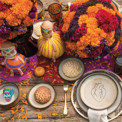 A colorful table setting featuring small ceramic skulls among other decorative items, representing a festive and artistic ambiance.