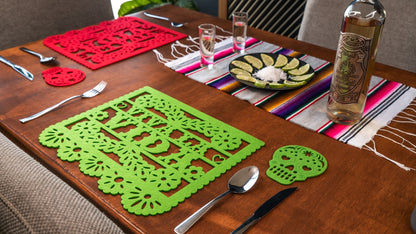 A set of colorful Mexican felt placemats on a wooden dining table, with cut-out designs resembling papel picado decorations.