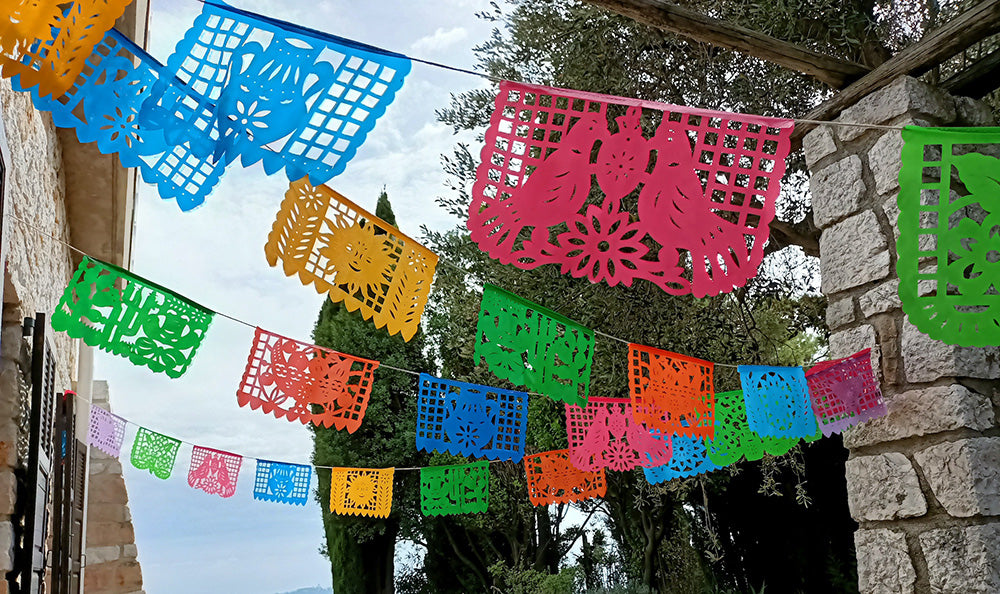A colorful outdoor party decoration setup with a series of plastic flags in various colors hanging along a rope, displayed over a table set for an outside event.