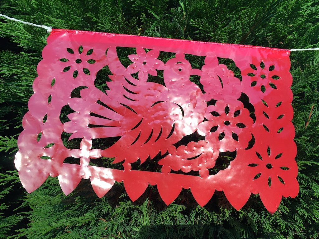 A colorful red plastic Mexican flag hanging along a rope to decorate an outdoor garden party.