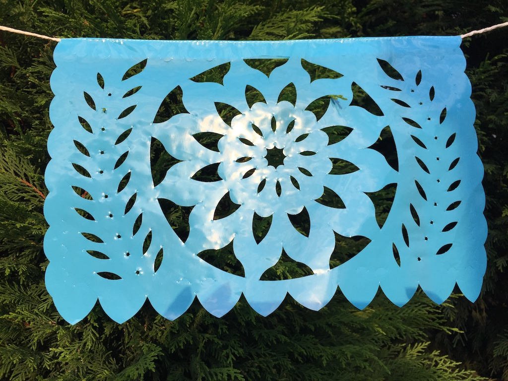 A colorful intricately cut blue plastic Mexican flag hanging on a rope, to decorate an outdoor garden party.